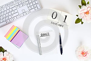 Write a goal for the new year 2010 in a white notebook on a white desktop next to a coffee mug and a keyboard. Top view, flat layo