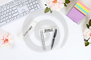 Write a goal for the new year 2010 in a white notebook on a white desktop next to a coffee mug and a keyboard. Top view, flat layo