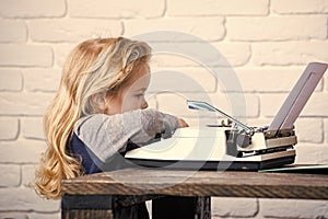 Writer kid sitting at table and typing typewriter with paper