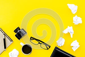 Writer office desk with notebook, ink, pen and glasses yellow background top view space for text