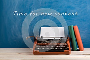 writer's workplace - red typewriter and stationery on blue blackboard background with text "Time for a new content