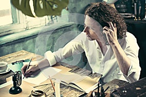 Writer at work. Handsome young writer sitting at the table and writing something in his sketchpad