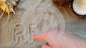 Writes the word relax, on the sand of the beach with a seashell and a coconut