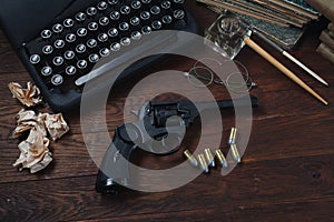 Writing a crime fiction story - old retro vintage typewriter and revolver gun with ammunitions, books, papers, old ink pen