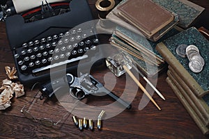 Writing a crime fiction story - old retro vintage typewriter and revolver gun with ammunitions, books, papers, old ink pen