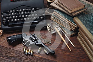 Writing a crime fiction story - old retro vintage typewriter and revolver gun with ammunitions, books, papers, old ink pen