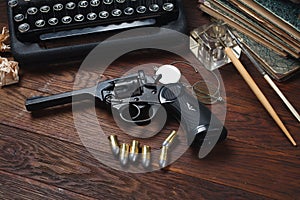 Writing a crime fiction story - old retro vintage typewriter and revolver gun with ammunitions, books, papers, old ink pen