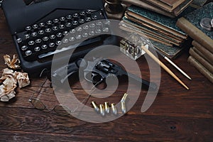 Writing a crime fiction story - old retro vintage typewriter and revolver gun with ammunitions, books, papers, old ink pen