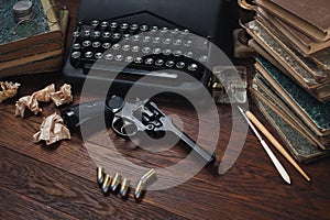 Writing a crime fiction story - old retro vintage typewriter and revolver gun with ammunitions, books, papers, old ink pen