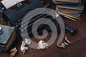 Writing a crime fiction story - old retro vintage typewriter and revolver gun with ammunitions, books, papers, old ink pen