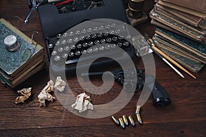 Writing a crime fiction story - old retro vintage typewriter and revolver gun with ammunitions, books, papers, old ink pen