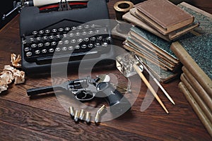 Writing a detective story - old retro vintage typewriter and revolver gun with ammunitions, books, papers, old ink pen