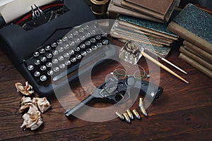 Writing a detective story - old retro vintage typewriter and revolver gun with ammunitions, books, papers, old ink pen