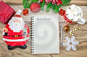 Writing a letter to Santa Claus on a wooden background with Christmas gifts, a plate in the shape of Santa Claus, a mug