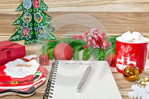 Writing a letter to Santa Claus on a wooden background with Christmas gifts, a plate in the shape of Santa Claus, a mug