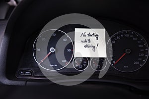 Writing no texting while driving on memo post reminder. Text on sticky paper inside car dashboard