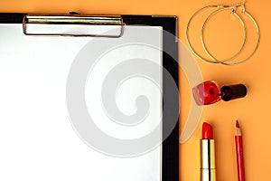 Writing pad with white sheet, next to red lipstick, red nail polish and round earrings. Notepad, to do list, get ready for date. A