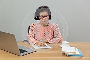 Writing After Retirement. Asian senior woman writer is writing details on book while working on laptop at home