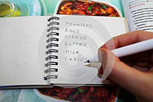 Writing shopping list for cooking meal by recipe. Food shopping concept