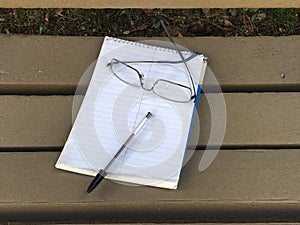 Writing tablet with black stick-pen and reading glasses.