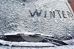 A writing `Winter` on a car windshield in a winter snowy day