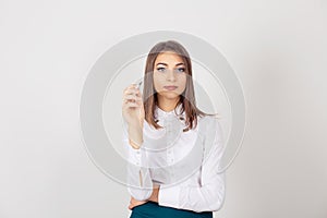 Writing. Young woman with elegant white shirt, holding ballpoint pen, looking to you camera, isolated white background, studio