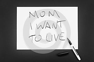 Written in black marker on a white piece of paper: Mom, I want to live