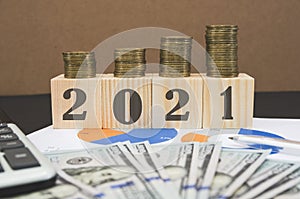 2021 is written on wood cubes on the background of business graphs and money. The stacks of coins on the dice are arranged in orde