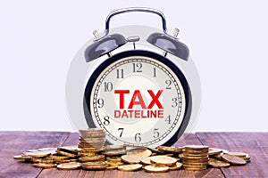 Written word Tax Dateline on a clock with gold coins on top of a