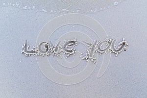 Written words `Love you` on sand of beach.