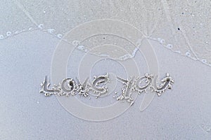 Written words `Love you` on sand of beach.