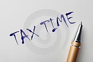 Written words TAX TIME and pen on white paper