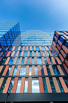 Upward view of a tall and modern office building full of glass windows reflecting the walls,