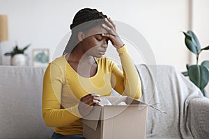 Wrong Package. Upset african american woman sitting with unpacked box at home