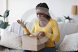 Wrong Parcel. Shocked frustrated black woman unpacking box, suffering from shipping mistake