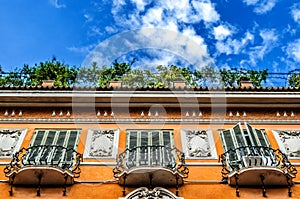 Wrought balconies on a beautiful orange building with green balconies on a blue sky background with fluffy blue clouds.