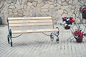 A wrought-iron bench stands on the sidewalk against a stone wall.A lonely wooden bench against a wall background, with