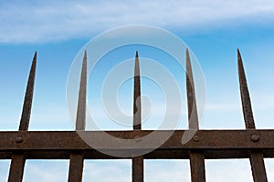 Wrought iron fence with sharp points on blue sky with clouds