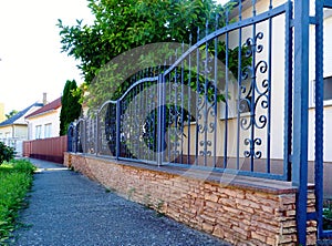 wrought iron fence between square stone piers and solid stone base. sidewalk with grass patch