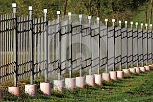 Wrought iron fence with vertical grey metal bars in a row mounted on concrete foundation surrounded with grass and fallen leaves