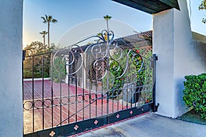 Wrought iron metal gate against red brick driveway of home with vines on trellis