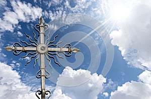 Wrought Iron Religious Cross on Beautiful Blue Sky with Clouds and Sun Rays