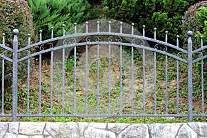 Wrought iron vintage retro dark grey fence with decorative elements on concrete wall covered with stone tiles foundation