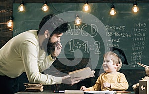 Wunderkind and genius concept. Father, teacher reading book, teaching kid, son, chalkboard on background. Dad wants to