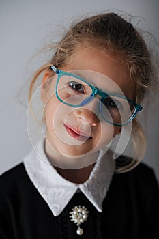 Wunderkind little caucasian girl in blue eyeglasses and school black and white uniform smiling portrait