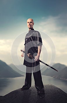 Wushu master with sword poses on top of mountain