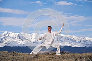 Wushu master in a white sports uniform training kungfu in nature on background of snowy mountains