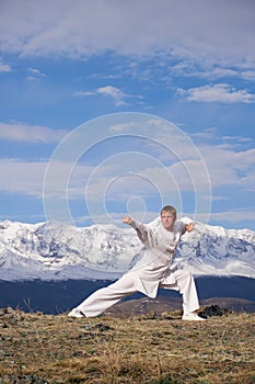 Wushu master in a white sports uniform training kungfu in nature on background of snowy mountains