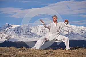 Wushu master in a white sports uniform training kungfu in nature on background of snowy mountains