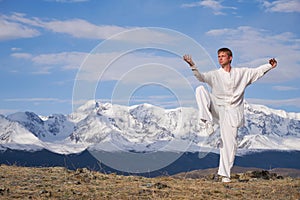 Wushu master in a white sports uniform training kungfu in nature on background of snowy mountains